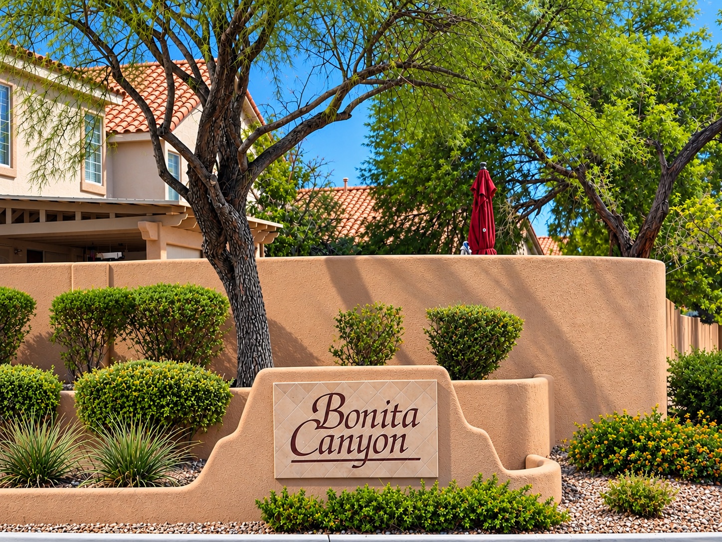 Bonita Canyon entrance monument with mature trees, desert landscaping, and tile-roof homes in The Pueblo, Summerlin